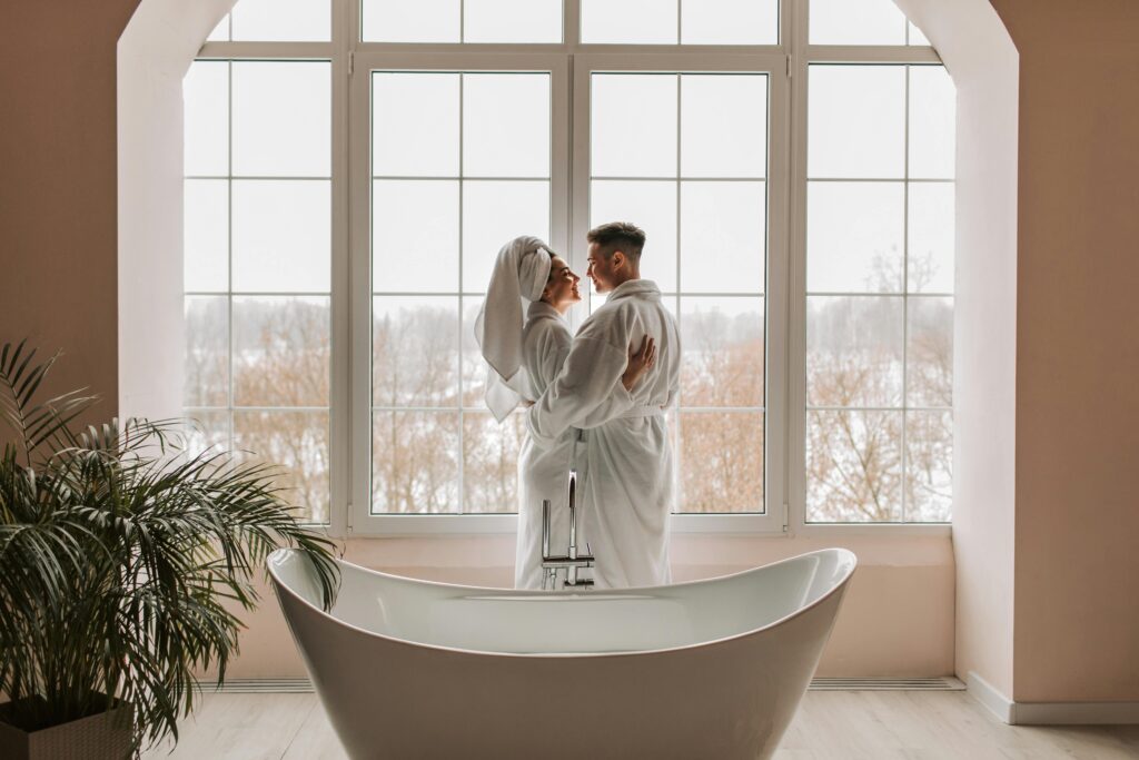 A loving couple in bathrobes share a moment of intimacy in a stylish bathroom by the window.